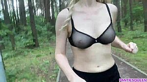 אישה בלונדינית מתאמנת בחוץ בפארק, חושפת את גופה העירום ושדיה המקפצים